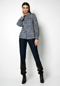 Gemusterte blaue und beige Bluse mit Kragen und langen Ärmeln, kombiniert mit dunklen Denim-Jeans und schwarzen kniehohen Stiefeln. Glatte Stofftextur.