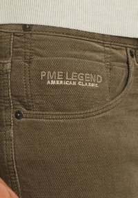 Zielone dżinsy bawełniane z teksturowanym wykończeniem, z haftowanym logo "PME LEGEND AMERICAN CLASSIC" w jasnobrązowym kolorze na tylnej kieszeni.