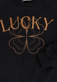 Zwarte sweater met grote gouden borduring van het woord "LUCKY" boven een klavervormig ontwerp met gebogen lijnen en details.