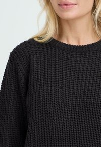 Czarny sweter dziany z teksturowanym, otwartym splotem. Posiada okrągły dekolt i długie rękawy. Miękki materiał o luźnym kroju.