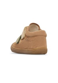 Chaussure en suède beige pour tout-petit avec deux bandes velcro, col rembourré doux et semelle en caoutchouc, présentée de dos et en vue latérale inclinée.