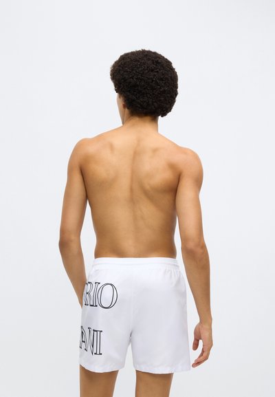 Άσπρα μαγιό βερμούδα με μαύρο κείμενο στο πλάι, με ελαστική μέση. Το ύφασμα φαίνεται λείο και ελαφρύ.