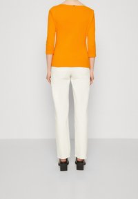 Orange-farbenes, tailliertes Oberteil mit weitem Halsausschnitt und drei Viertel-Ärmeln, kombiniert mit off-white geraden Hosen und klobigen Absatzschuhen.
