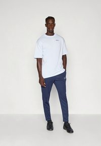 Camiseta de manga corta azul claro con un pequeño logo, combinada con pantalones deportivos navy que tienen un diseño blanco en forma de swoosh. Zapatillas negras.