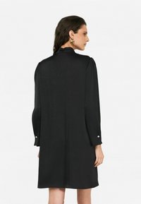 Abito nero con maniche a sbuffo lunghe, dettaglio posteriore con un motivo sottile e bottoni decorativi ai polsini. Tessuto di texture liscia.