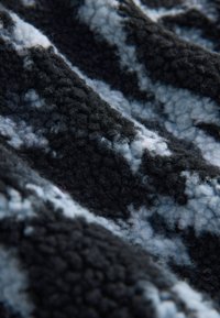 Gestructureerde stof met een zwarte basis en wit-grijze abstracte patronen, die een zachte, pluizige uitstraling en een golvend vallend draag toont.