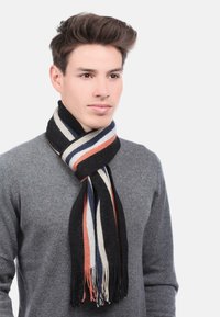 Écharpe en laine avec des rayures verticales noires, navy, orange et crème, avec des bords frangés. Associée à un pull gris.