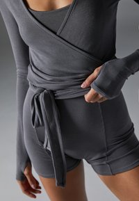 Sivý ribovaný outfit s obvodovým dizajnom, dlhými rukávmi, otvormi pre palce a detailom s viazaním v páse. Šortky sú priliehavé a bezšvové.