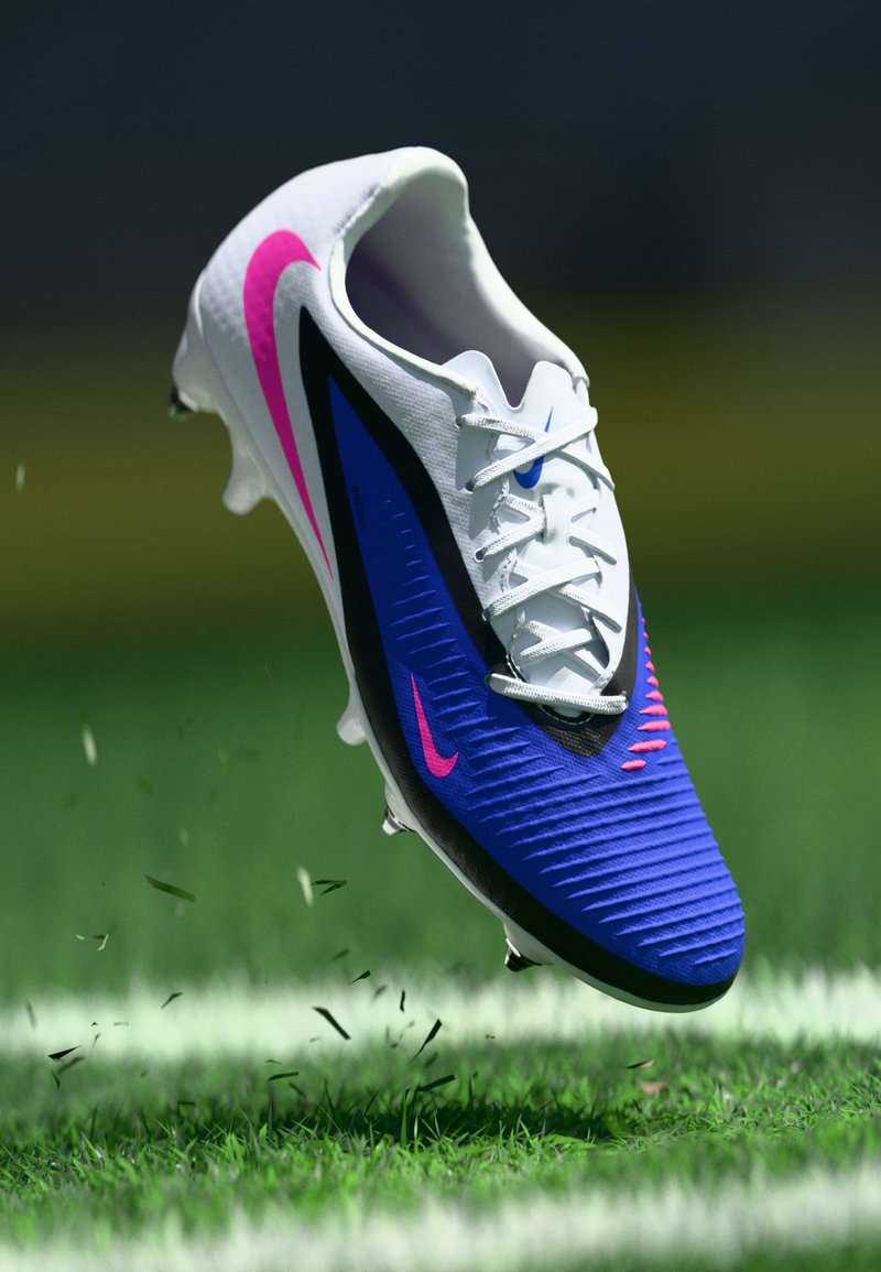 Ποδοσφαιρικό παπούτσι Nike με λευκό επάνω μέρος, μπλε υφή, ροζ πινελιές και μαύρες λεπτομέρειες. Διαθέτει κορδόνια και κράμα καρφιών.