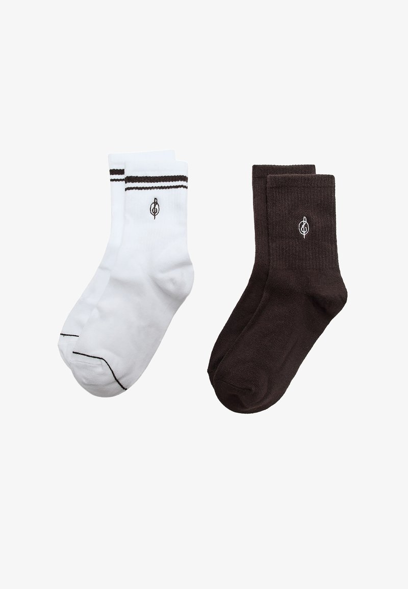 Due paia di calzini alla caviglia, uno bianco con strisce nere e logo, l'altro nero con logo bianco, esposti su uno sfondo bianco semplice.
