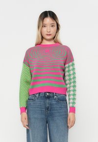Pulover tricotat cu dungi orizontale roz și verde, mâneci cu model contrastant în zigzaguri verzi și houndstooth roz, cu manșete ribbate.