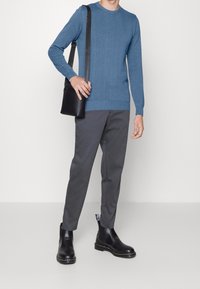 Pull en maille bleu clair avec un motif zigzag texturé, pantalon gris fuselé et bottines Chelsea noires brillantes avec des bandes latérales. Sac bandoulière noir.
