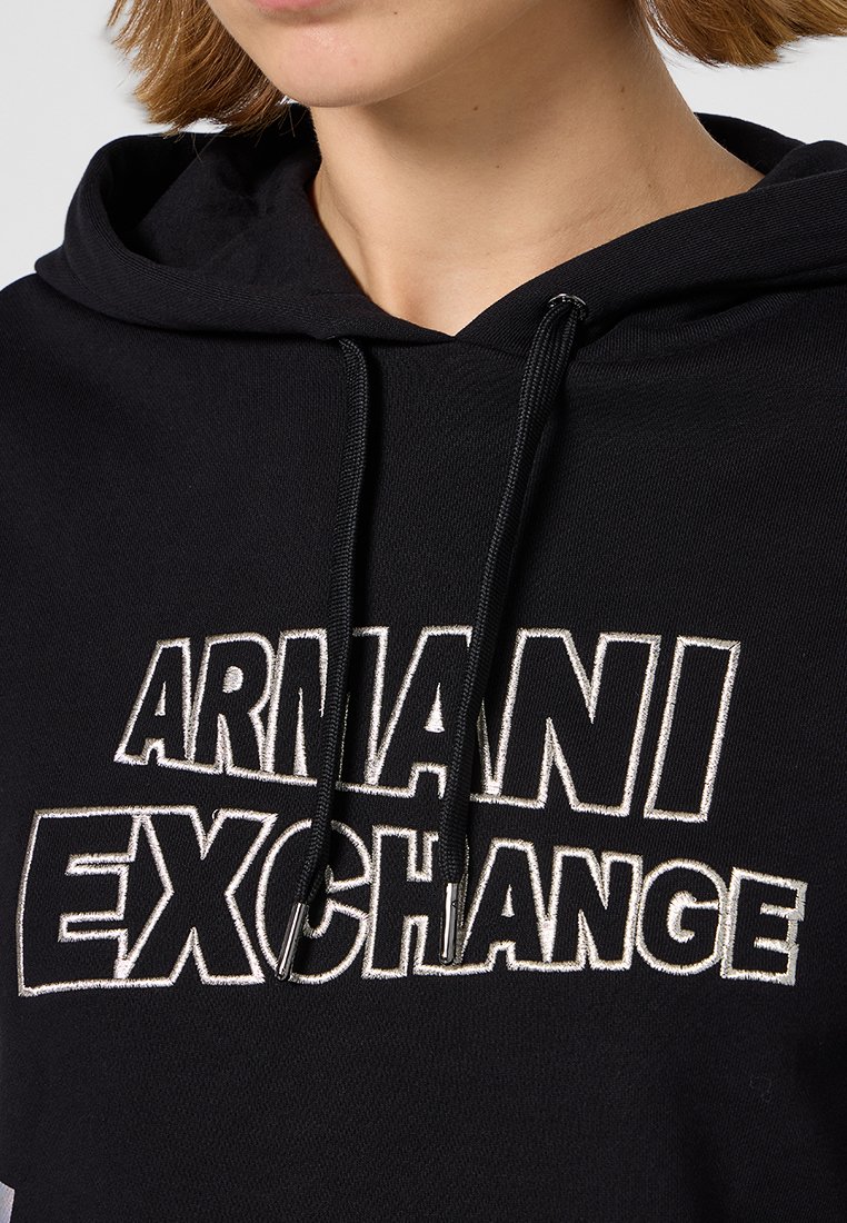 Sudadera negra con capucha y texto bordado en blanco "ARMANI EXCHANGE". Presenta un cordón y tejido texturizado. Primer plano del cuello.