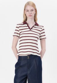 Kurzärmliges, V-Ausschnitt-T-Shirt in Off-White mit kastanienbraunen Streifen. Stricktextur, gerippter Kragen. Kombiniert mit dunkel gefütterten Hosen mit doppelten Knöpfen.