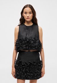 Conjunto preto de duas peças consistindo numa blusa sem mangas e uma saia mini, ambos adornados com apliques florais em camadas e um acabamento de textura suave.