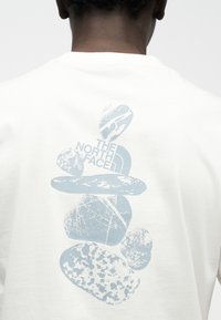 Λευκό βαμβακερό μπλουζάκι με ανοιχτό μπλε γραφικό στοιχείο που απεικονίζει στοιβαγμένες πέτρες και κείμενο που γράφει "THE NORTH FACE" στην πλάτη.