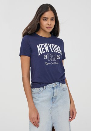 T-shirt di cotone blu navy con maniche corte, con testo stampato bianco: "NEW YORK 1995 USA Upper East Side." Abbinato a una gonna di denim chiaro.