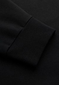 Nahaufnahme von schwarzem Stoff, der den gerippten Abschluss eines Langarms hervorhebt und Textur- sowie Nähdetails zeigt.