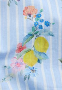 Kaks kollast sidrunit rohelistes lehtedes, ümbritsetud roosade, siniste ja oranžide lilledega helesinisel ja valgel triibulisel kangal.