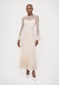 Duga, prozirna, svijetloružičasta haljina s točkicama, uska haljina, raširene rukave i slojevita suknja; uparena s bijelim, špicastim cipelama.