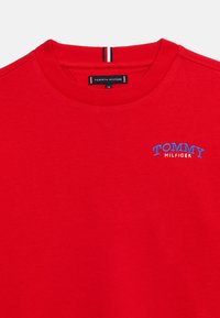 Κόκκινο φούτερ με στρογγυλή λαιμόκοψη και κεντημένο μπλε και λευκό λογότυπο "Tommy Hilfiger" στο στήθος, με ετικέτα της μάρκας στο εσωτερικό του γιακά.