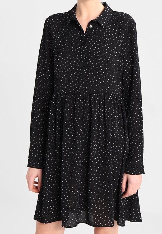 Robe noire à manches longues, col et taille froncée. Présente un motif à pois gris clair. Tissu léger et fluide.
