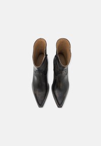 Bottines en cuir noir avec un bout pointu, présentant une légère finition usée et des accents de couture décorative. Intérieur doublé de matière beige.