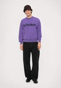 Violetinė palaidinė su juodu užrašu "No Problemo", derinama su laisvomis juodomis kelnėmis ir juodais sportbačiais. Minimalistinis stilius, kasdieniškas siluetas.