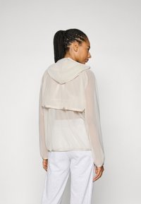 Lätt, genomskinlig beige jacka med huva, långa ärmar och en kortad ryggdesign, med en mjuk textur och avslappnad passform.