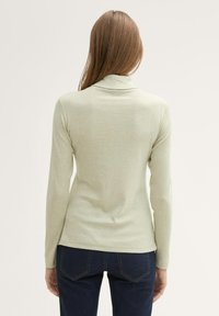 Helles grünes Langarmoberteil mit Stehkragen und tailliertem Design, aus weichem Stoff hergestellt. Die Rückansicht zeigt eine glatte Textur und subtile Nähte.