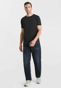 T-shirt nera a maniche corte abbinata a jeans blu scuro. Il modello indossa sneaker grigie chiare. Design semplice e casual con una vestibilità rilassata.