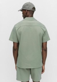 Chemise verte à manches courtes en tissu texturé, avec un col et des détails cousus, associée à un short assorti, vue de dos.