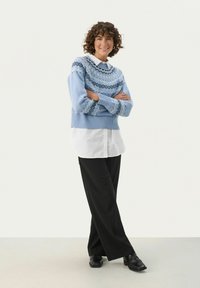 Light blue knitted sweater with geometric patterns, layered over a white button-up shirt; paired with black wide-leg trousers and black shoes.