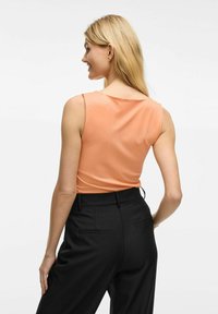 Top portocalie fara maneci, cu decolteu rotund, asortat cu pantaloni negri croiti, evidentiind o textura neteda si linii clare.