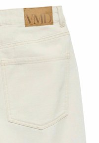 Poche arrière d'un jean en denim blanc cassé avec une pièce en cuir marron cousue au-dessus, embossée des lettres "VMD".