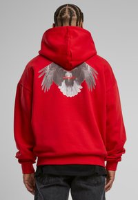 Felpa con cappuccio rossa caratterizzata da un grande grafiche delle ali di un'aquila sul retro. Realizzata in tessuto morbido con una vestibilità comoda e polsini a costine.