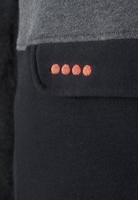 Tessuto nero con una superficie liscia presenta un inserto grigio nella parte superiore. Cinque punti rossi ricamati sono visibili sulla porzione nera.