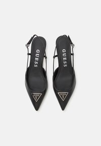 Melnas slingback papēžu kurpes ar norādītām purngalām, gludas ādas materiāls un trīsstūrveida logo akcenta sudraba krāsā. Aprīkotas ar regulējamu siksnu.