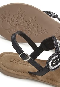 Sandalo nero con decorazioni in perline, fibbia regolabile, soletta in morbido suede beige e suola in gomma con motivo.