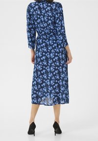 Navy sininen kukallinen mekko, jossa on kolme neljännestä hihaa, vyötärö kireällä ja virtaava hame, joka ulottuu puoleen pohkeeseen, yhdistettynä mustiin korkokenkiin.