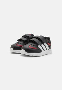 Zapatillas deportivas negras con rayas blancas, correas de Velcro y acentos rojos. Hechas de material sintético, presentan una parte superior texturizada y una suela de goma.