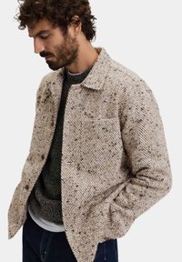 Beige jasje met visgraatpatroon, gemaakt van textuurstof, met een gespreid kraag, een knoopsluiting aan de voorkant en zijzakken.