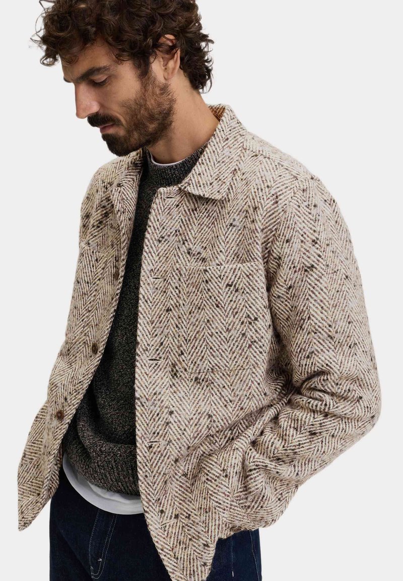 Beige jasje met visgraatpatroon, gemaakt van textuurstof, met een gespreid kraag, een knoopsluiting aan de voorkant en zijzakken.