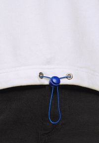 Vêtements blancs avec un cordon de serrage en bas, des fermetures bleu à travers des œillets en argent, et une texture en coton lisse.