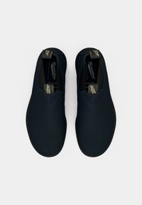 Para granatowych butów wsuwanych z czarnymi podeszwami i markowymi pętlami na białym tle, widziana z góry.