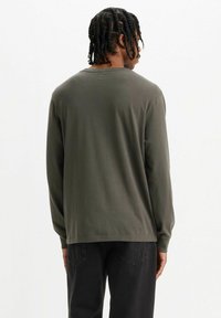 Długo-sleeve oliwkowa zielona koszula wykonana z miękkiej bawełny, z okrągłym dekoltem i luźnym krojem. Widok z tyłu ukazuje gładki, płaski dół.