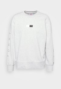Sudadera gris de mezcla de algodón, con cuello redondo, puños acanalados, un parche rectangular de logo en blanco y negro, y texto "TOMMY" en la manga.