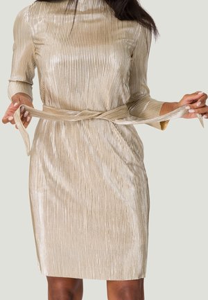 Robe à côtes en or métallique avec manches longues, silhouette ajustée, et ceinture nouée à la taille. Texture lisse avec un éclat réfléchissant.