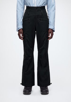 Le mannequin porte un pantalon cargo noir à jambes larges, taille haute, avec des poches zippées et des bas resserrables par cordon, associé à une chemise bleu pâle et à des chaussures foncées.