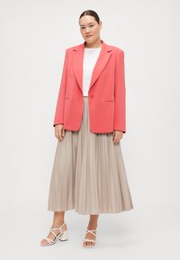 Korallfarget blazer med notched krage, kombinert med en hvit topp og et plisserte beige midi-skjørt. Strappy hvite hæler fullfører antrekket.